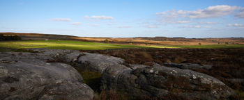 Peak district wide This image is a landscape photograph depicting the Peak District in Derbyshire, United Kingdom, with Curbar Edge in the foreground. Captured during an autumn afternoon, the scene features rugged rock formations characteristic of the area, surrounded by rolling rural fields and open moorland, under a sky dotted with clouds. The photograph conveys the natural beauty and varied terrain of the Peak District, highlighting its importance as a nature reserve and a rural escape in the heart of Derbyshire.